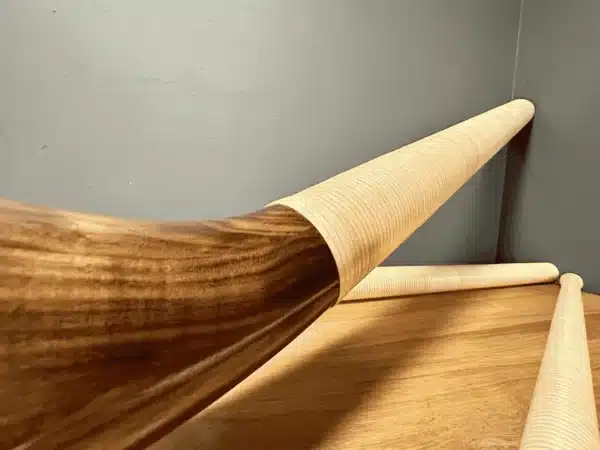 Hochwertige Alphörner aus Holz, kombiniert mit präzise gefertigten Mundstücken, auf einem Holztisch vor blauer Wand.