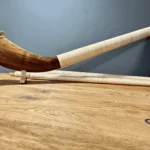 Alphorn mit schön gemasertem Schallstück und natürlichem Holzmundstück auf Holzoberfläche, NATURINSTRUMENTE Heimatklang.