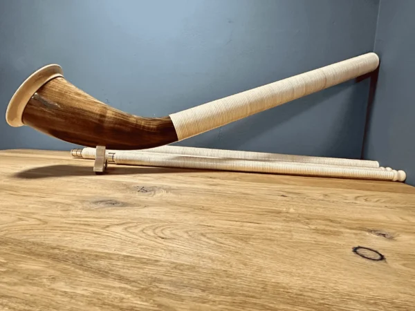 Alphorn mit schön gemasertem Schallstück und natürlichem Holzmundstück auf Holzoberfläche, NATURINSTRUMENTE Heimatklang.