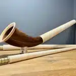 Alphorn aus edlem Holz mit zwei Teilen und feinen Mundstücken, präsentiert auf einem Holzuntergrund.
