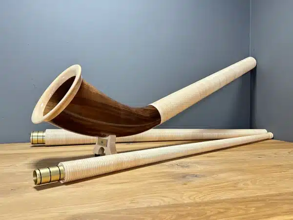 Alphorn aus edlem Holz mit zwei Teilen und feinen Mundstücken, präsentiert auf einem Holzuntergrund.