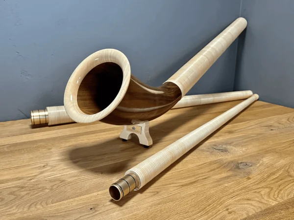 Alpenhorn aus edlem Holz auf Holztisch dargestellt, mit Details der feinen Struktur, für Naturinstrumente-Enthusiasten.