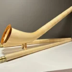Alphorn aus hellem Holz mit Mundstück auf weißem Tisch, präsentiert von NATURINSTRUMENTE Heimatklang für authentischen Klang.