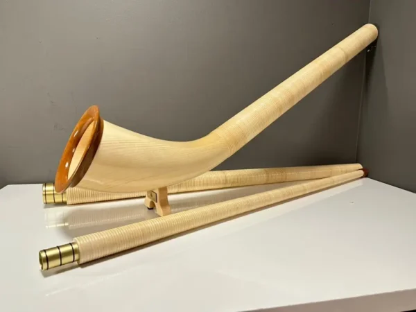 Alphorn aus hellem Holz mit Mundstück auf weißem Tisch, präsentiert von NATURINSTRUMENTE Heimatklang für authentischen Klang.