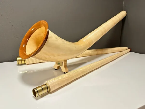 Alpenhorn in edlem Holzdesign mit passenden Mundstücken, präsentiert auf einem Tisch, betont Handwerkskunst und Klangqualität.