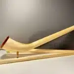 Alphorn in Einzelteilen mit präzise gearbeiteten Holzmundstücken auf weißem Tisch, präsentiert vor grauer Wand.