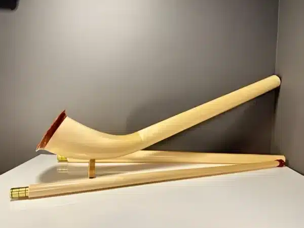 Alphorn in Einzelteilen mit präzise gearbeiteten Holzmundstücken auf weißem Tisch, präsentiert vor grauer Wand.