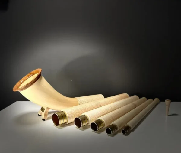 Set alpiner Alphorn-Segmente und Holzmundstück auf Tisch, beleuchtet, symbolisiert handwerkliche Qualität und Naturklang.