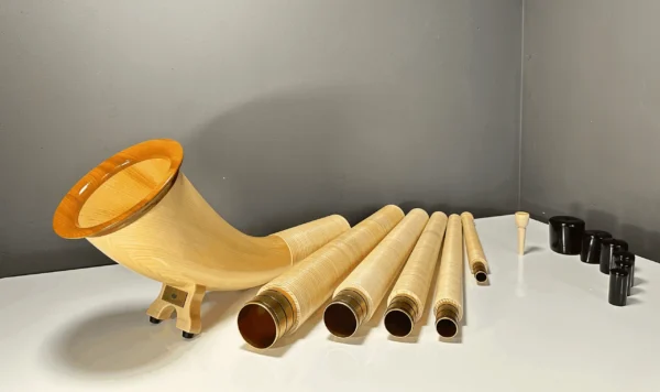 Alphorn aus hellem Holz mit Mundstücken, zerlegt, auf weißem Tisch präsentiert. Hochwertige Handwerkskunst von NATURINSTRUMENTE Heimatklang.