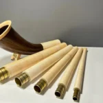 Alpenhorn aus Holz mit mehreren Mundstücken, präsentiert auf einem Tisch; ideal zur Darstellung von Naturinstrumenten bei Heimatklang.