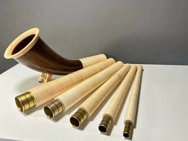 Alpenhorn aus Holz mit mehreren Mundstücken, präsentiert auf einem Tisch; ideal zur Darstellung von Naturinstrumenten bei Heimatklang.