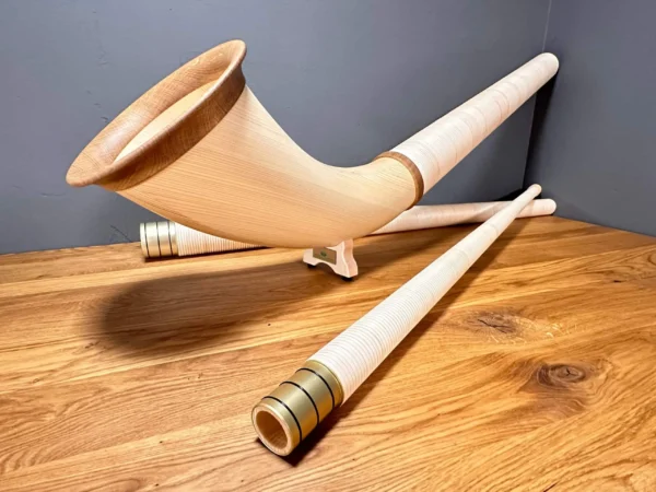 Handgefertigte Alphörner mit edlen Holzmundstücken auf Holztisch, ideal für authentische Heimatklänge von NATURINSTRUMENTE.