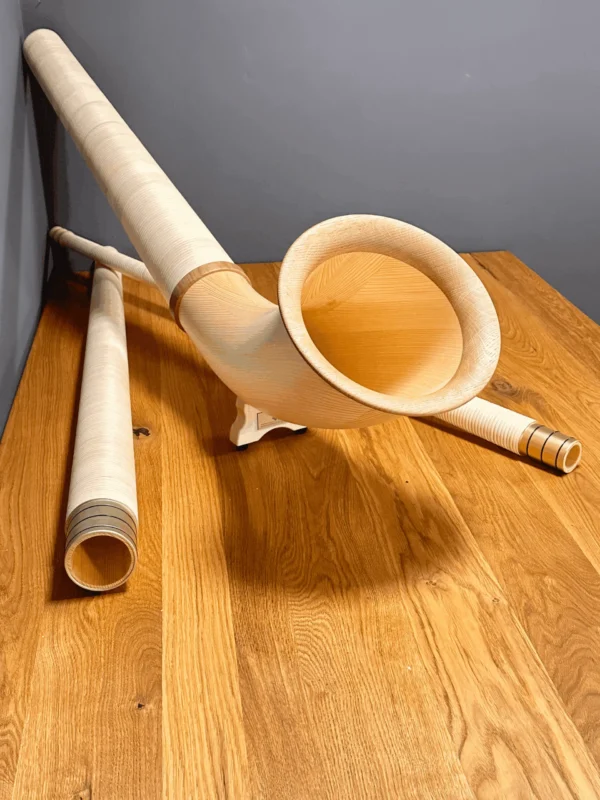 Alphorn und Holzmundstücke auf Holztisch zeigen traditionelle Handwerkskunst von NATURINSTRUMENTE Heimatklang.