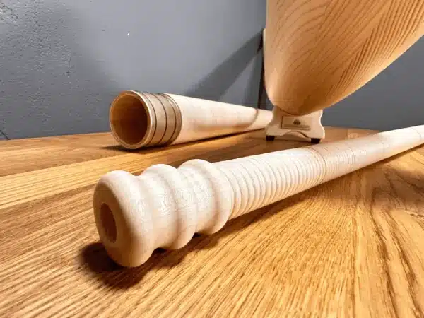 Alphorn und zwei präzise gefertigte Holzmundstücke auf Holzuntergrund, Fokus auf handwerkliche Qualität von Naturinstrumenten.