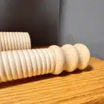 Handgefertigte, geriffelte Holzmundstücke für Alphörner liegen auf einem Holztisch, ideal für Heimatklang-Enthusiasten.