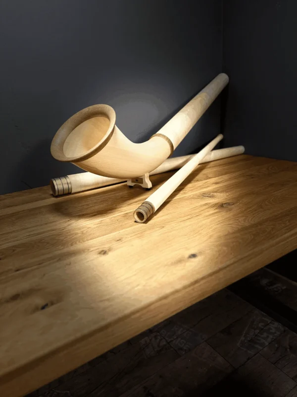 Hochwertiges Alphorn auf Holztisch, zeigt die feine Handwerkskunst von NATURINSTRUMENTE für authentischen Heimatklang.