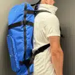 Ein Mann trägt eine blaue Tasche für Alphörner auf dem Rücken, perfekt für den Transport von hochwertigen Alpenhorn-Mundstücken.