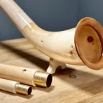 Edles Alphorn aus Holz mit goldenen Mundstücken, präsentiert auf einem Holztisch. Perfekt für den Heimatklang traditioneller Musik.