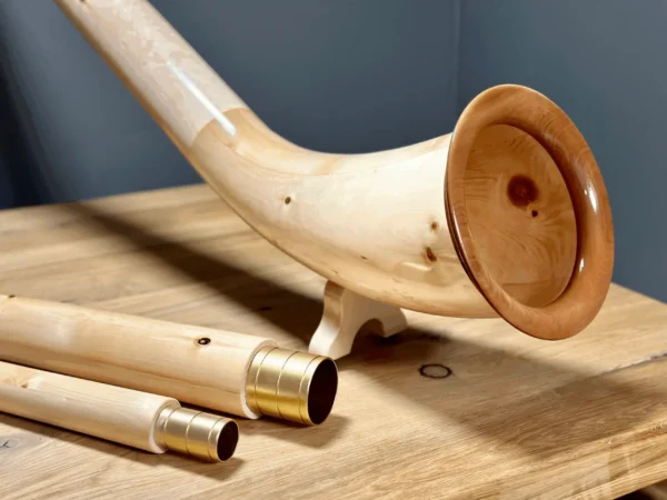 Edles Alphorn aus Holz mit goldenen Mundstücken, präsentiert auf einem Holztisch. Perfekt für den Heimatklang traditioneller Musik.