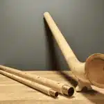 Alphorn aus Holz und passende Mundstücke auf Holztisch, präsentiert von NATURINSTRUMENTE Heimatklang.