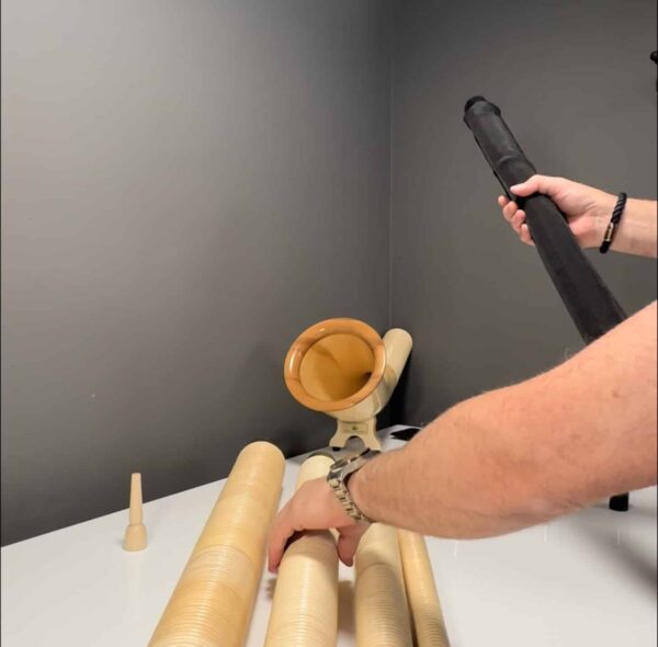 Ein Mann montiert hochwertige Alphornteile und Holzmundstück auf einem Tisch, in einer Werkstatt für Naturinstrumente.