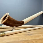 Alphorn mit kunstvoll gefertigten Holzmundstücken, auf Holzboden präsentiert, zeigt traditionelle Handwerkskunst.