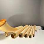 Alpenhorn mit abnehmbaren Holzsegmenten und Mundstück, präsentiert auf einem weißen Tisch vor grauer Wand.