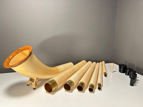 Alpenhorn mit abnehmbaren Holzsegmenten und Mundstück, präsentiert auf einem weißen Tisch vor grauer Wand.