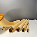 Alphorn in Einzelteile zerlegt mit edlen Holzmundstücken, präsentiert auf weißem Tisch vor grauer Wand.