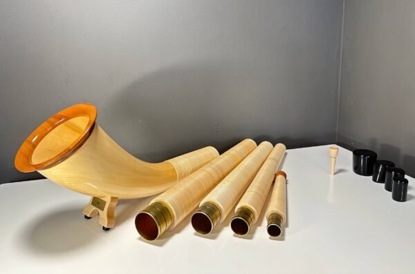 Alphorn in Einzelteile zerlegt mit edlen Holzmundstücken, präsentiert auf weißem Tisch vor grauer Wand.