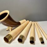 Hochwertige Alphornsegmente und Holzmundstücke auf weißer Fläche, präsentiert für „NATURINSTRUMENTE Heimatklang“.