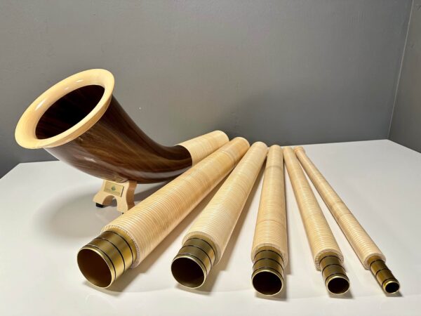 Hochwertige Alphornsegmente und Holzmundstücke auf weißer Fläche, präsentiert für „NATURINSTRUMENTE Heimatklang“.