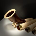 Hochwertige Alphörner und Holzmundstücke, präsentiert auf dunklem Hintergrund, Produkte von NATURINSTRUMENTE Heimatklang.