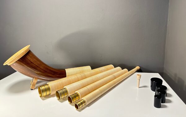 Alphorn mit mehreren Rohren, Holzmundstück und Zubehör in einem Raum auf einem Tisch ausgelegt, zeigt handwerkliche Qualität.
