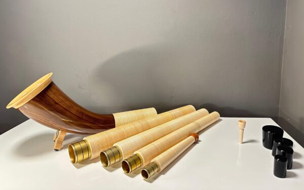 Alpenhorn mit handgefertigten Holzmundstücken und Zubehör, präsentiert auf einem Tisch, ideal für Liebhaber von Naturinstrumenten.