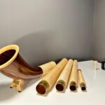 Alpenhorn mit Holzstücken auf weißem Tisch, hochwertige Mundstücke für Naturinstrumente bei NATURINSTRUMENTE Heimatklang.