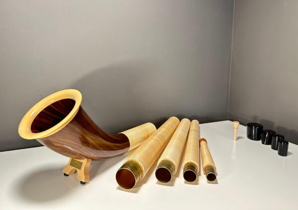Alpenhorn mit Holzstücken auf weißem Tisch, hochwertige Mundstücke für Naturinstrumente bei NATURINSTRUMENTE Heimatklang.