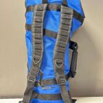 Blauer Rucksack mit schwarzen Gurten für den Transport von Alpenhörnern und Mundstücken, stehend auf einem Tisch.