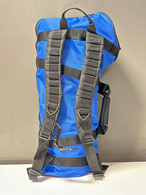 Blauer Rucksack mit schwarzen Gurten für den Transport von Alpenhörnern und Mundstücken, stehend auf einem Tisch.