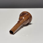 Handgefertigtes Holzmundstück für Alphörner, präsentiert auf einer weißen Fläche, spiegelt traditionelle Handwerkskunst wider.