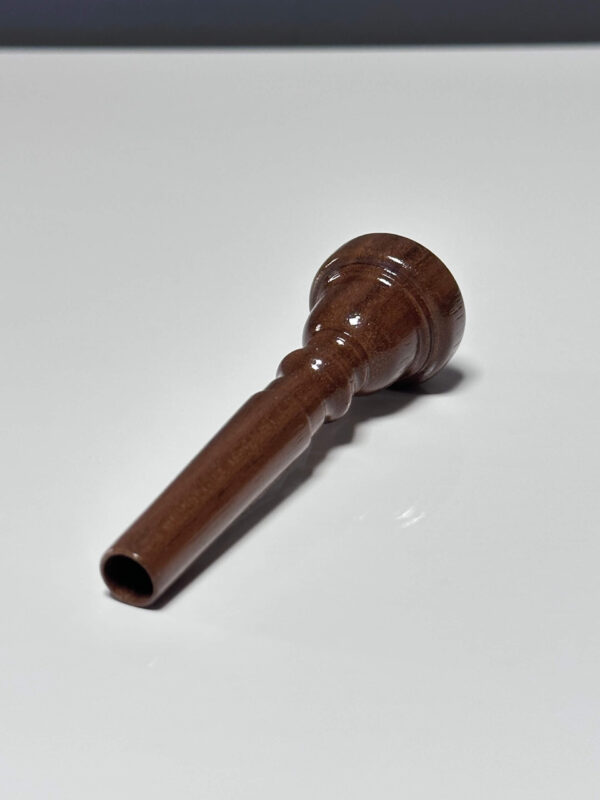 Fein gearbeitetes Holzmundstück für Alphörner, präsentiert auf einer weißen Oberfläche, symbolisiert naturnahen Klang.
