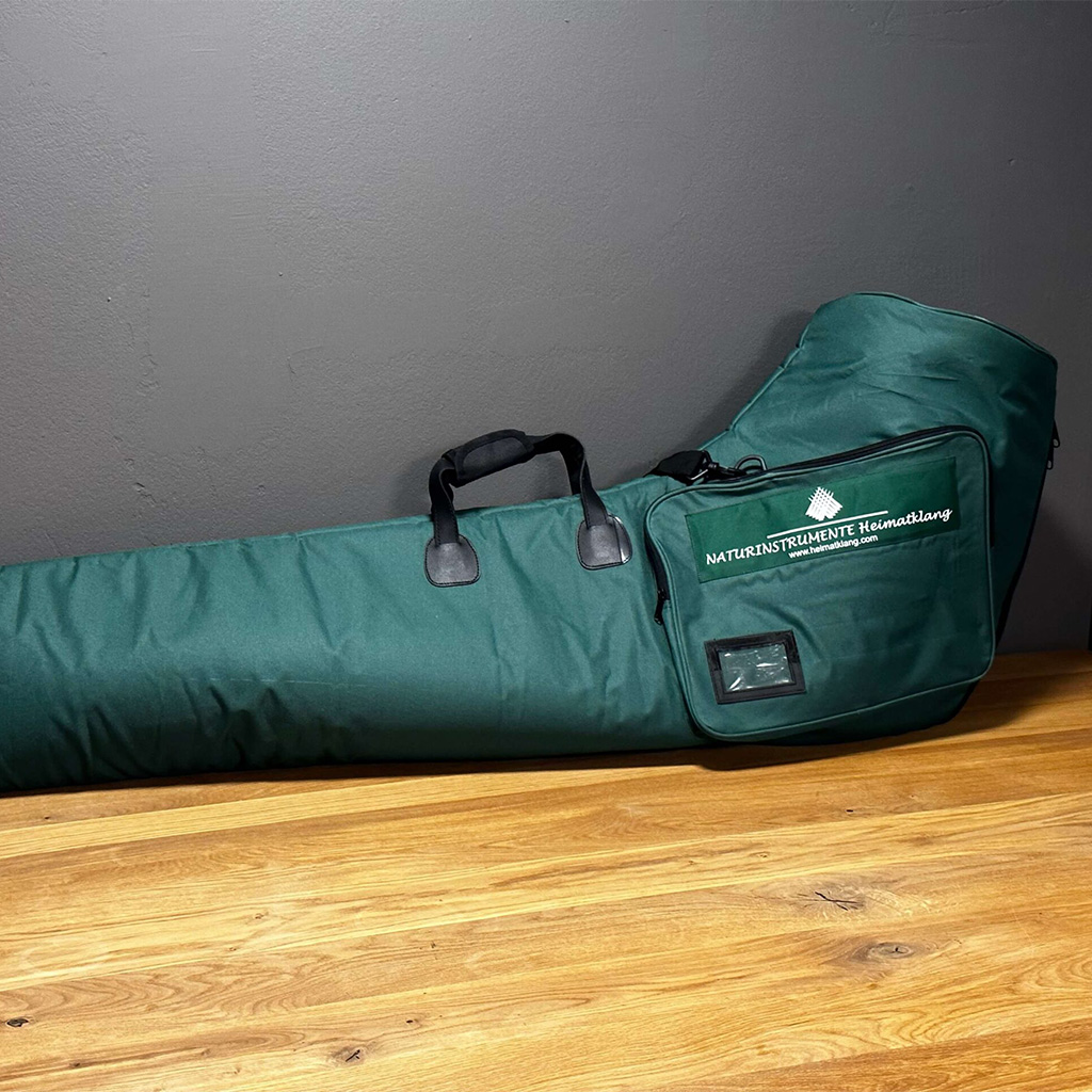 Grüne Tasche für Alphörner von NATURINSTRUMENTE Heimatklang auf Holztisch mit Logo und Tragegriffen.