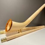 Alphorn mit detailreichem Holzmundstück, elegant auf einem Tisch arrangiert, zeigt die Handwerkskunst von Heimatklang Naturinstrumente.