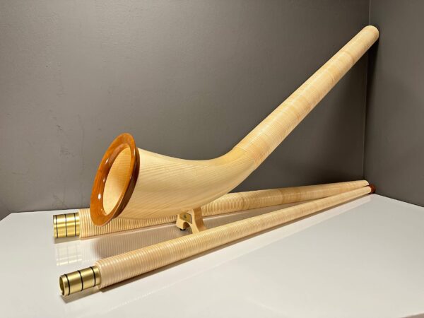 Alphorn mit detailreichem Holzmundstück, elegant auf einem Tisch arrangiert, zeigt die Handwerkskunst von Heimatklang Naturinstrumente.