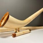 Alphorn aus hellem Holz mit edlen Mundstücken, präsentiert auf einer glänzenden Oberfläche. Ideal für Heimatklang-Enthusiasten.