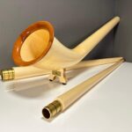 Alphorn mit edlen Holzmundstücken auf weißer Oberfläche vor grauer Wand, symbolisiert hochwertige Handwerkskunst.