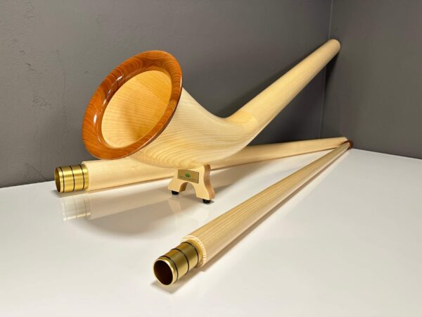 Alphorn mit edlen Holzmundstücken auf weißer Oberfläche vor grauer Wand, symbolisiert hochwertige Handwerkskunst.