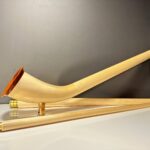 Hochwertiges, naturbelassenes Alpenhorn mit Mundstück, präsentiert auf einem weißen Tisch vor neutralem Hintergrund.