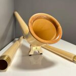 Alphorn aus hellem Holz mit separaten Mundstücken, präsentiert auf einem weißen Hintergrund. Eleganz und Tradition vereint.