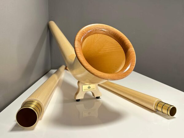 Alphorn aus hellem Holz mit separaten Mundstücken, präsentiert auf einem weißen Hintergrund. Eleganz und Tradition vereint.